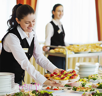 A server setting a dessert plate on a banquet table full of other food.