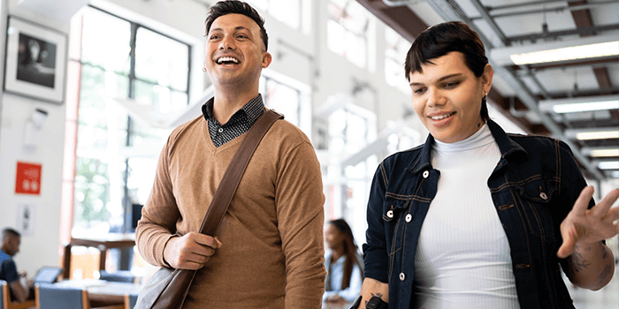 Two educators walking through a library, smiling, and enjoying their conversation.